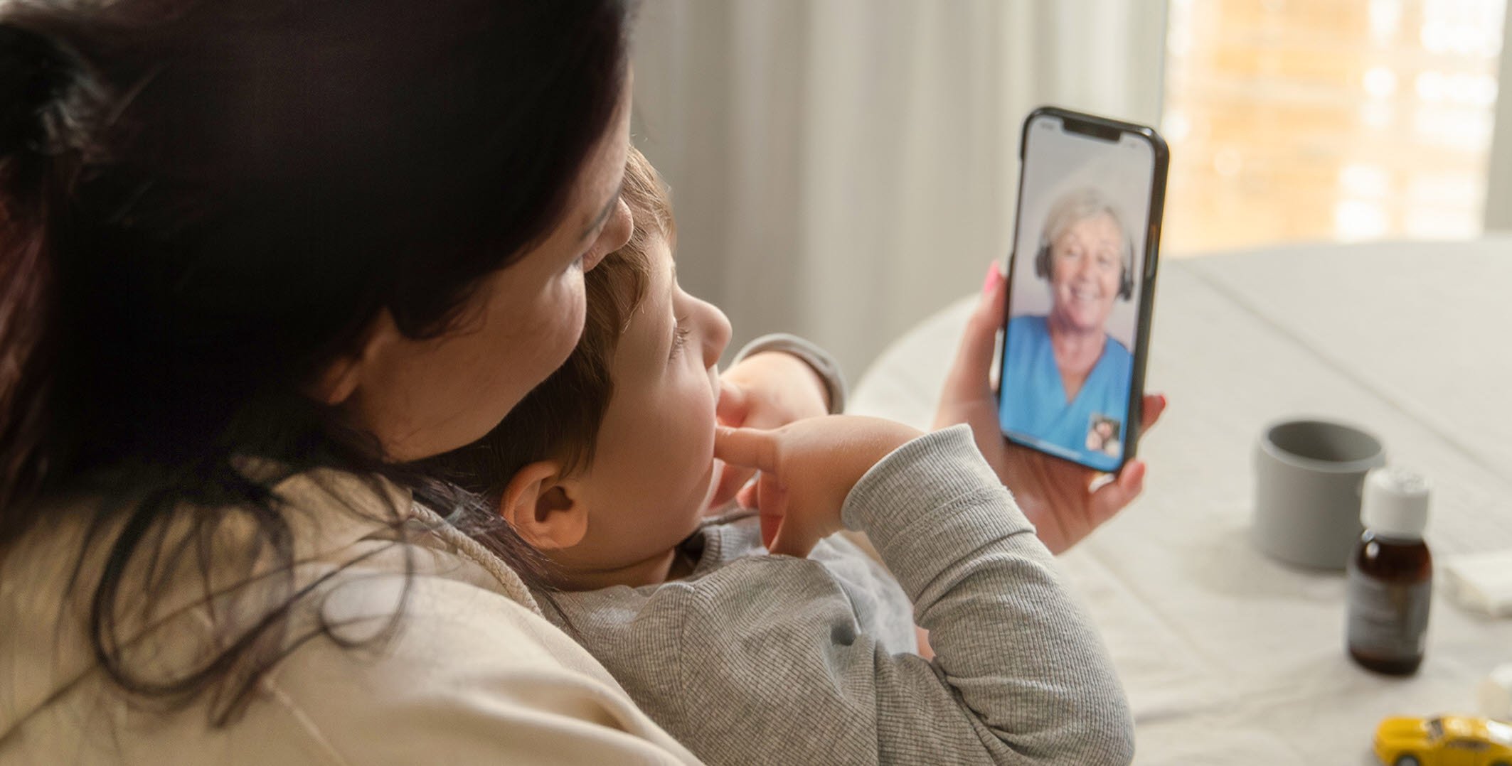 Barn som sitter i kvinnas famn. Pratar med Min vård Gävleborg i telefon.